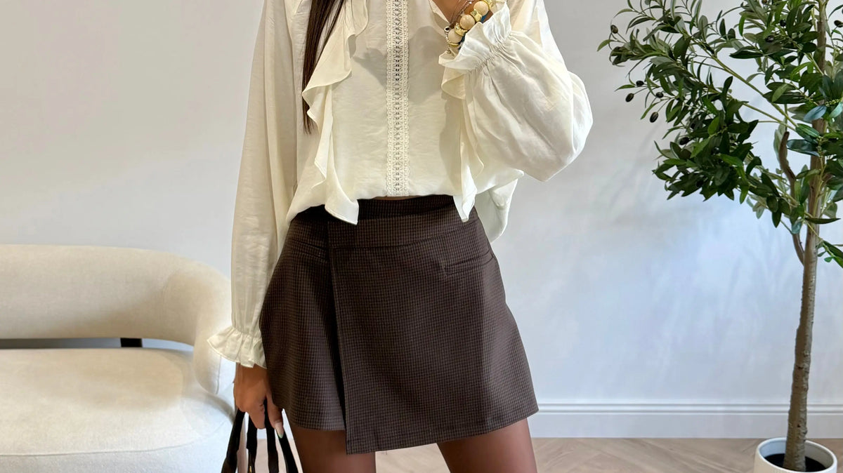 Femme portant des bottes marron avec une jupe courte chocolat, une blouse écrue et un sac à main marron.