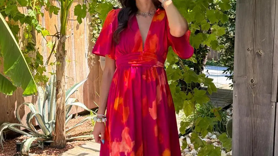 Robe longue rose fuchsia à motifs orange, portée avec des sandales et des lunettes de soleil dans un jardin.