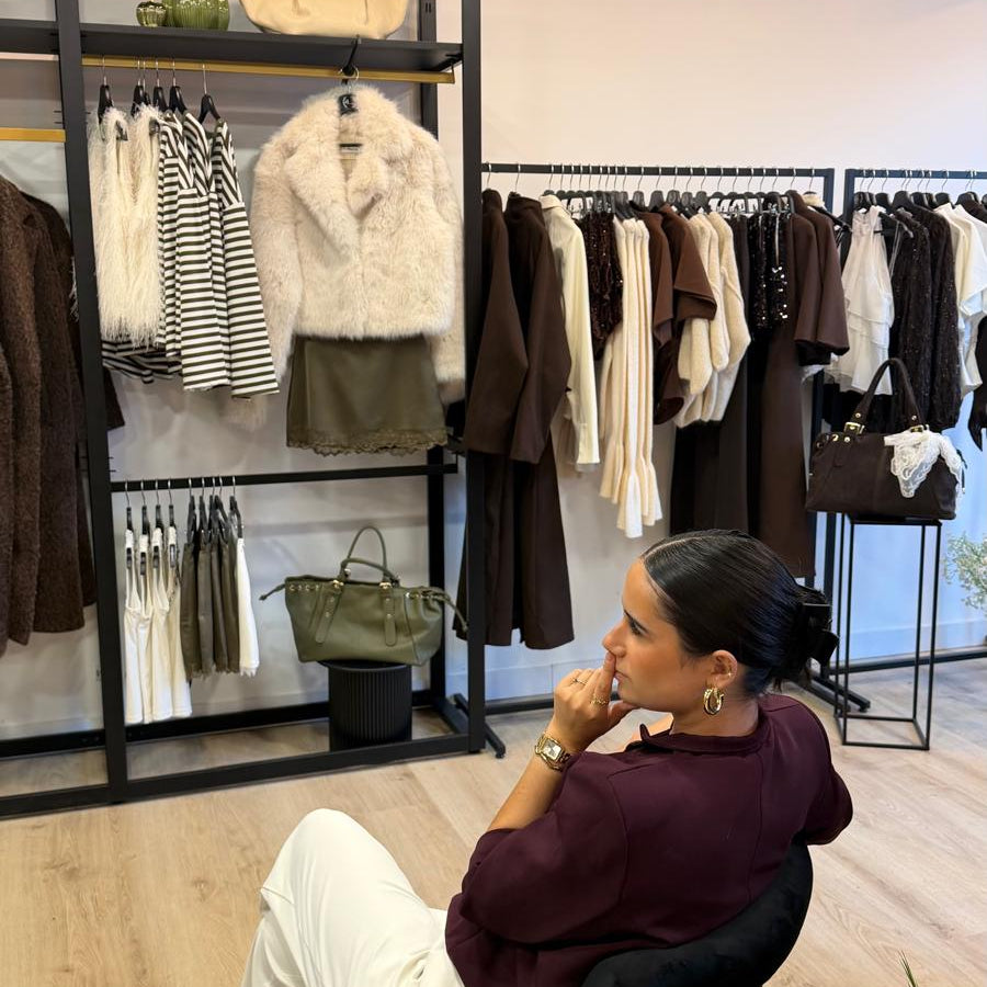 Femme assise dans la boutique DS Sélection, devant des portants de vêtements et des étagères de sacs à main.