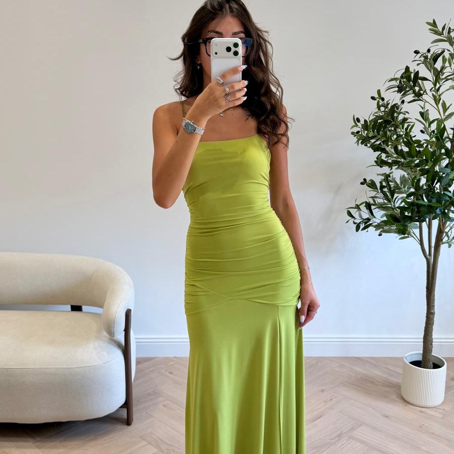 Femme portant une robe longue vert anis à fines bretelles, drapée à la taille, devant un miroir.