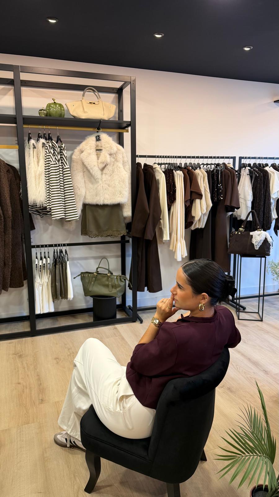 Femme assise dans la boutique DS Sélection, devant des portants de vêtements et des étagères de sacs à main.